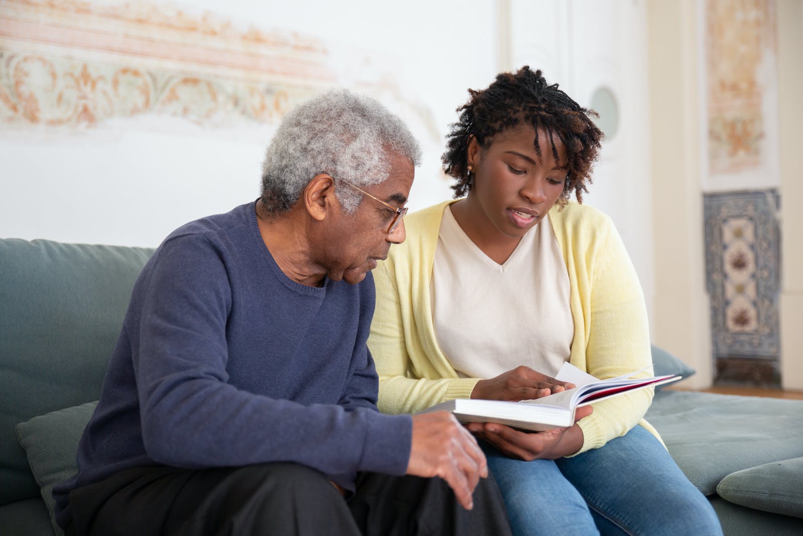 A Woman Reading a Book while Sitting Beside the Man in Blue Sweater